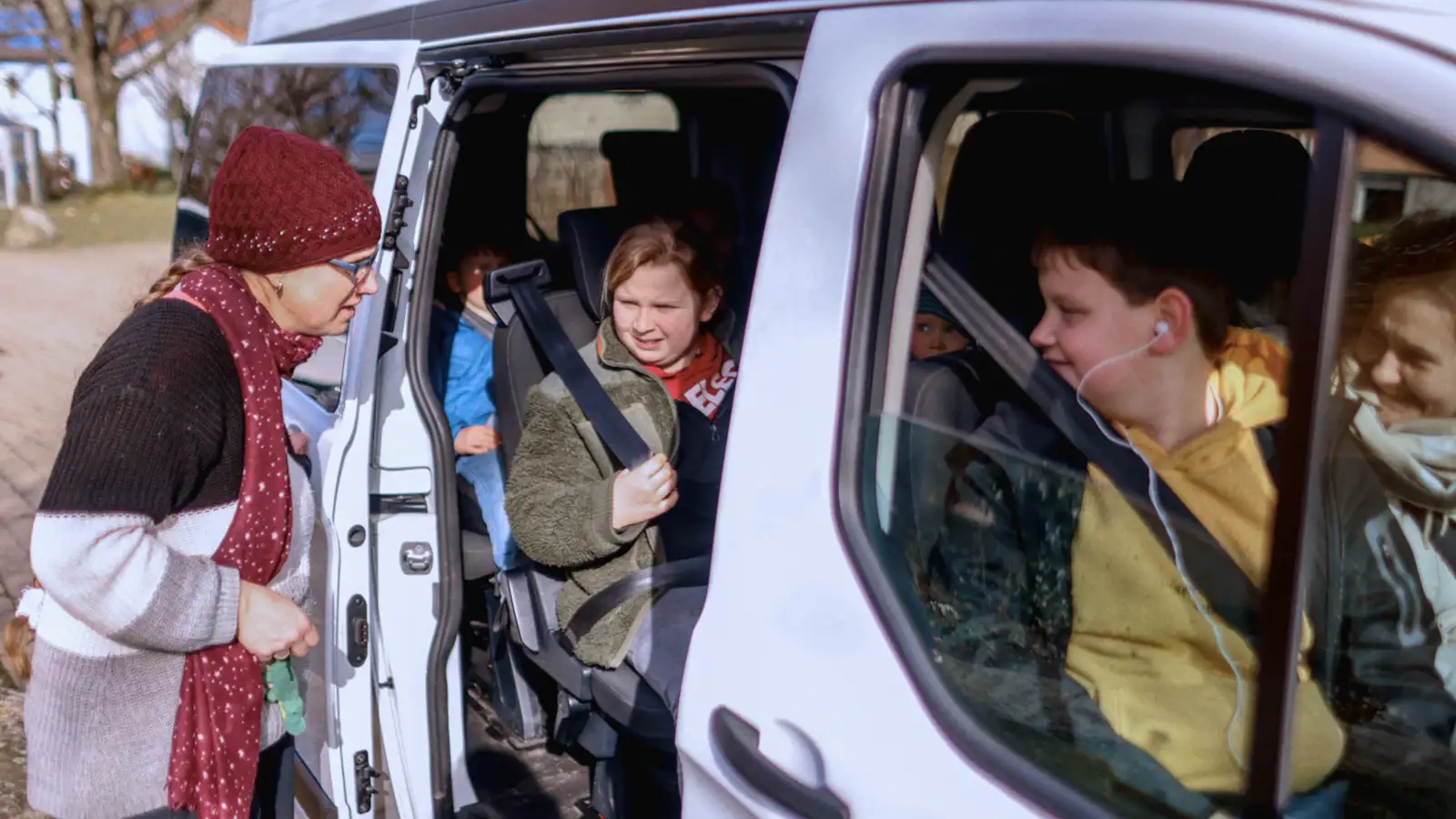 Eine Frau öffnet die Schiebetür eines Transporters, damit eine Jugendliche aussteigen kann.