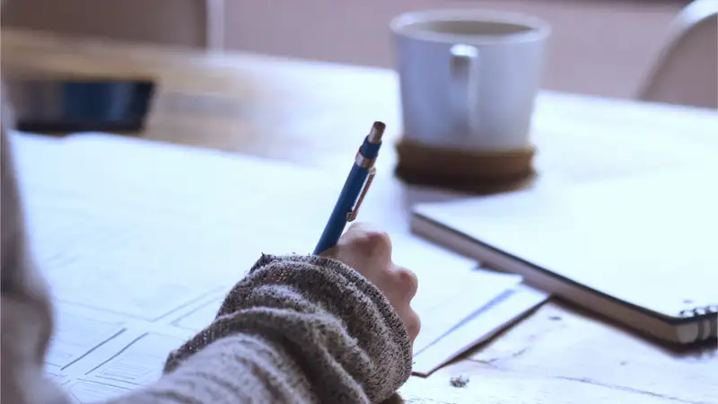 Eine Person mit einem Stift in der Hand sitzt an einem Tisch und macht Skizzen.