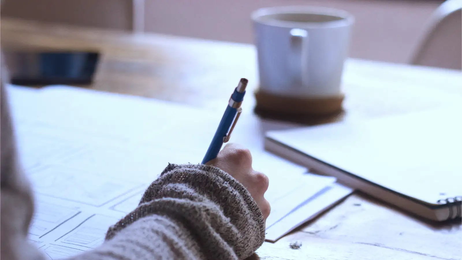 Eine Person mit einem Stift in der Hand sitzt an einem Tisch und macht Skizzen.