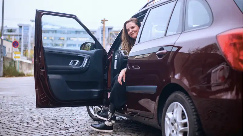 Eine Frau sitzt bei geöffneter Fahrertür im Auto und blickt nach draußen.