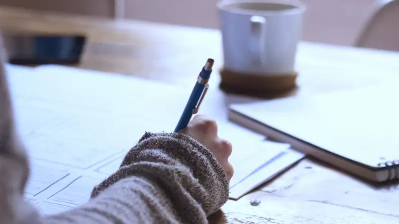 Eine Person mit einem Stift in der Hand sitzt an einem Tisch und macht Skizzen.