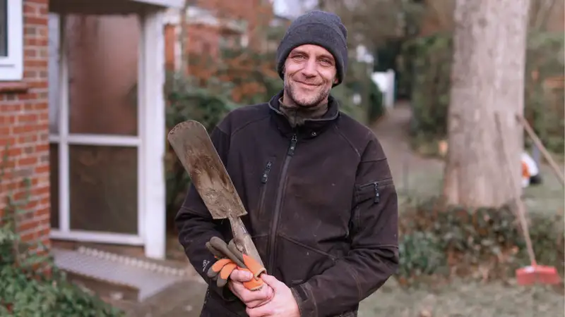 Ein lächelnder Mann in einem Garten mit einem Spaten in der Hand