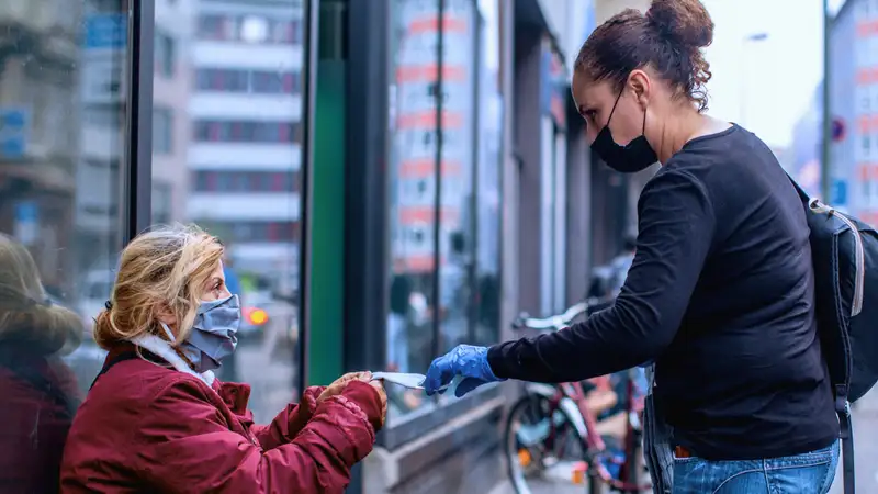 Eine junge Frau reicht einer Frau ohne Obdach einen Gegenstand.