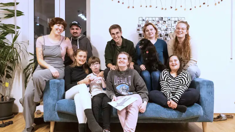 Eine neunköpfige Gruppe von Menschen mit und ohne Behinderung auf einem Sofa