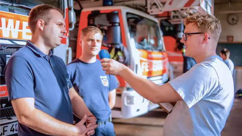 Zwei Feuerwehrleute werden von einem Mann mit Mikrofon interviewt