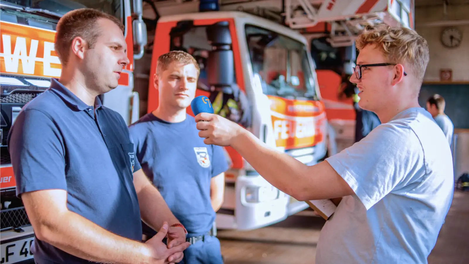 Zwei Feuerwehrleute werden von einem Mann mit Mikrofon interviewt