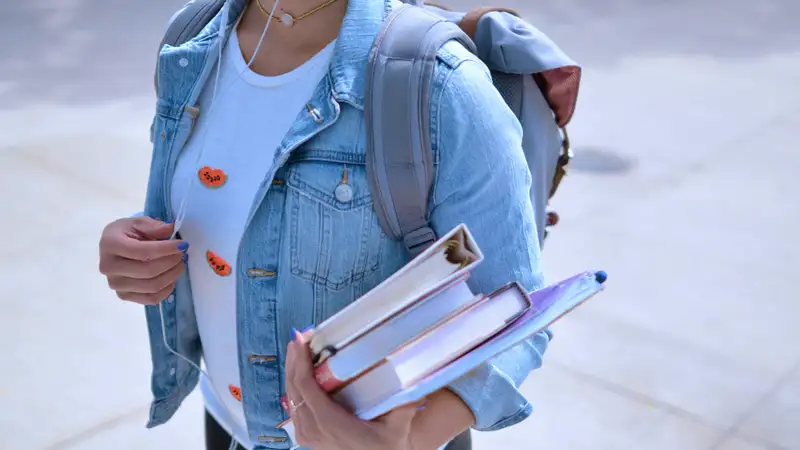 Eine Schülerin mit Rucksack und Büchern im Arm