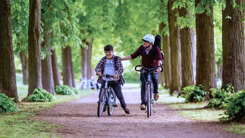 Zwei Männer auf Fahrrädern in einer Allee