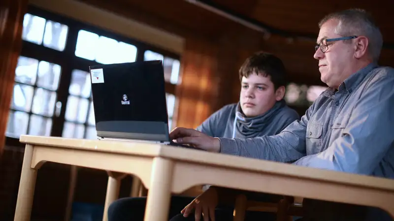 Ein Junge und ein Mann sitzen vor einem Laptop.