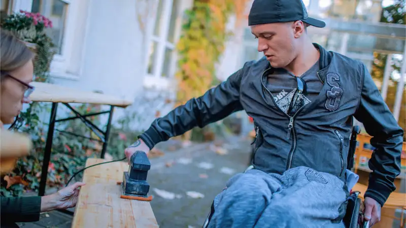 Ein junger Mann im Rollstuhl schleift ein Brett