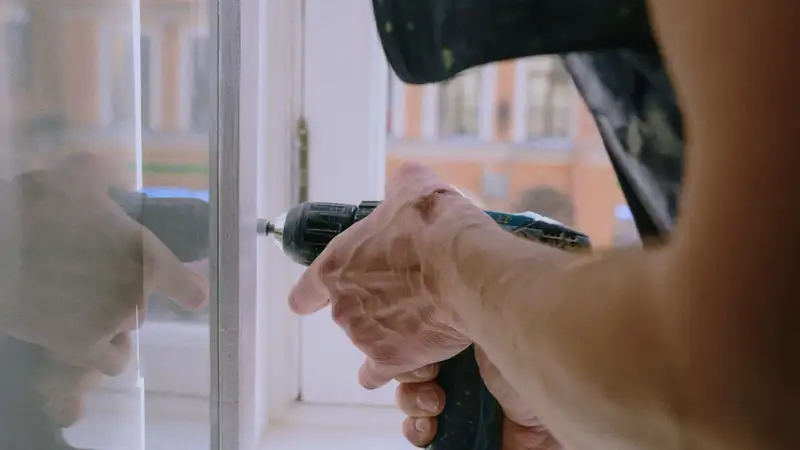 Eine Person mit einem Akkuschrauber an einem Fenster