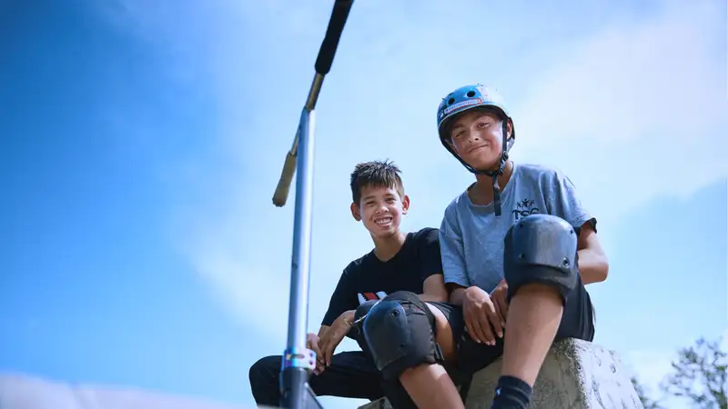 Zwei Skater sitzen oben auf einer Halfpipe und schauen nach unten