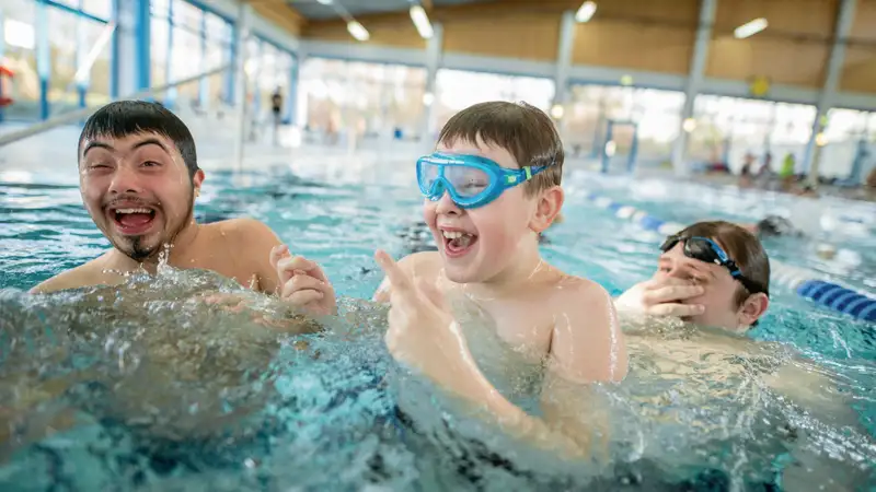Drei junge Menschen lachen im Wasser eines Hallenbads