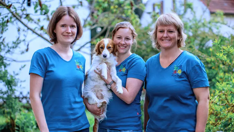 Drei Frauen, eine hält einen mittelgroßen Hund in den Armen.