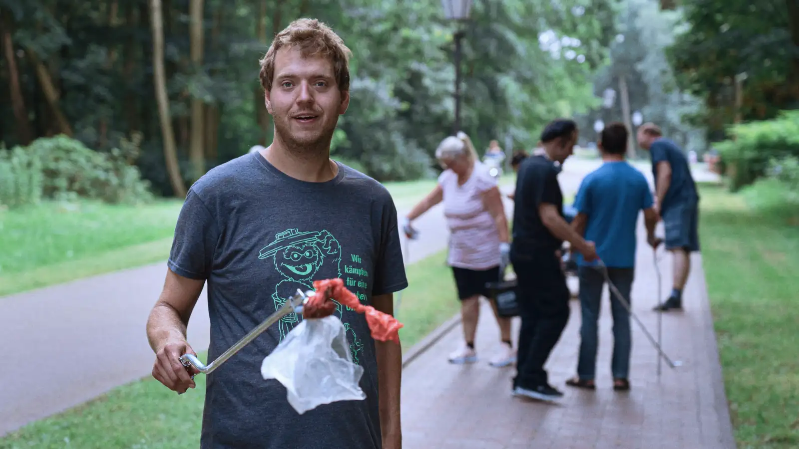 Ein junger Mann beim Müllsammeln im Park, hält mit der Zange eine Plastiktüte.