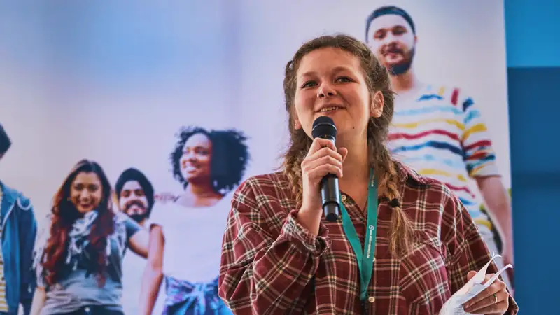 Eine junge Frau mit Mikrofon spricht auf einer Veranstaltung