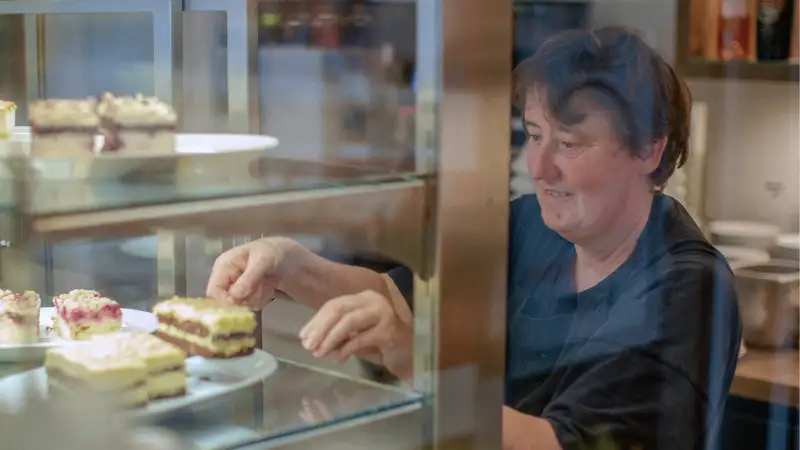 Eine Frau schiebt Kuchen in eine verglaste Auslage.