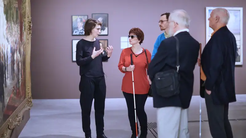 Eine Führerin im Museum erläutert einer Gruppe mit sehbehinderten Menschen ein Bild.