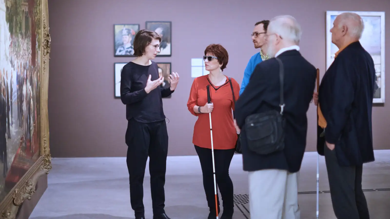 Eine Führerin im Museum erläutert einer Gruppe mit sehbehinderten Menschen ein Bild.