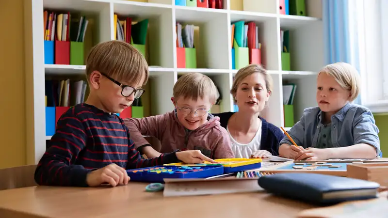 Drei Kinder im Grundschulalter lernen miteinander und werden dabei von einer erwachsenen Frau begleitet.