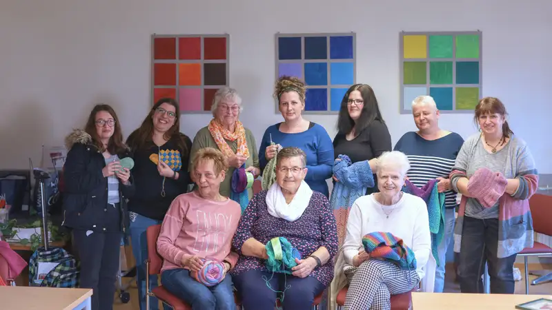 Eine Gruppe von Frauen zeigen verschiedene selbstgestrickte Dinge.