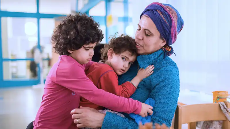 Eine Mutter kümmert sich um ihre zwei Kindern, die sich an sie schmiegen.