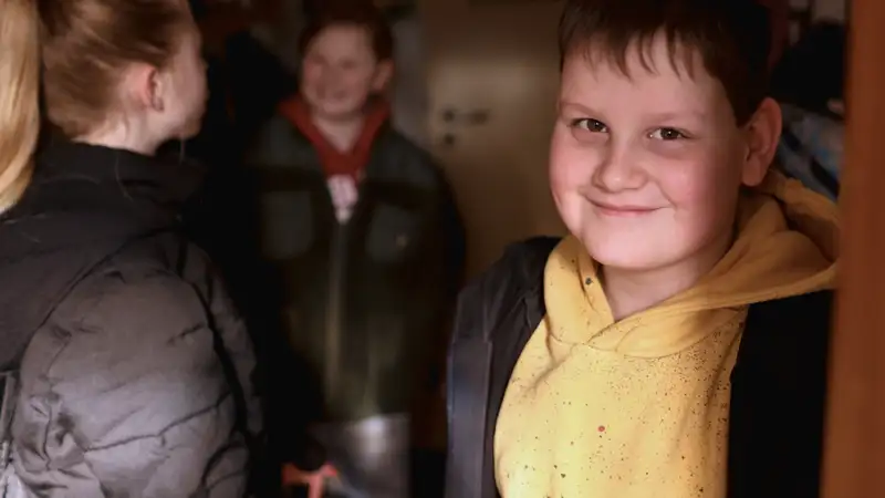 Ein lächelnder Junge im gelben Hoodie steht im Eingang eines Zimmers