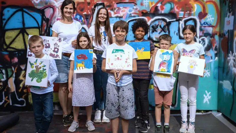 Eine Gruppe von Kindern mit ihren Begleiterinnen zeigen ihre selbstgemalten Bilder.