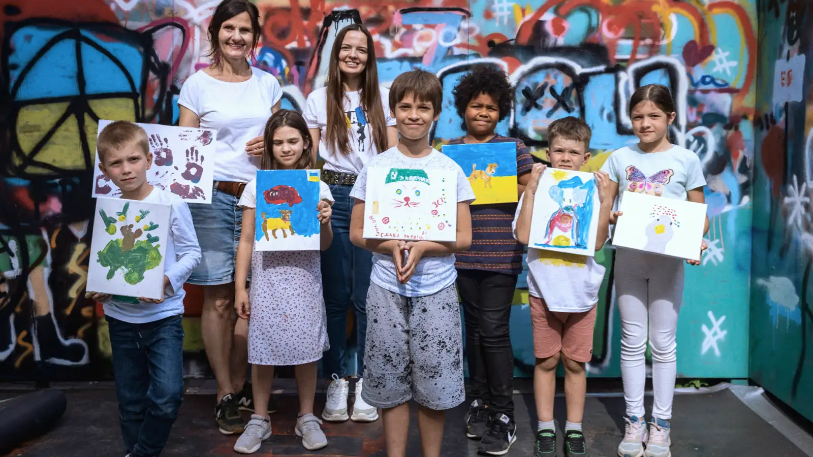 Eine Gruppe von Kindern mit ihren Begleiterinnen zeigen ihre selbstgemalten Bilder.
