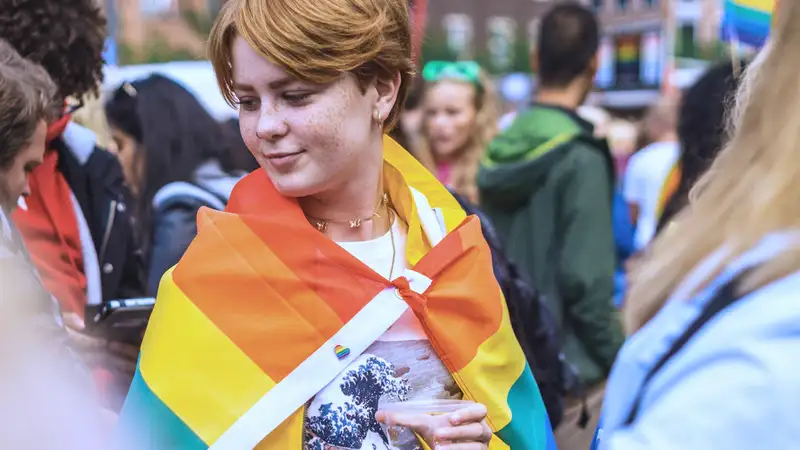 Ein junger Mensch mit einer umgehängten Regenbogenfahne.