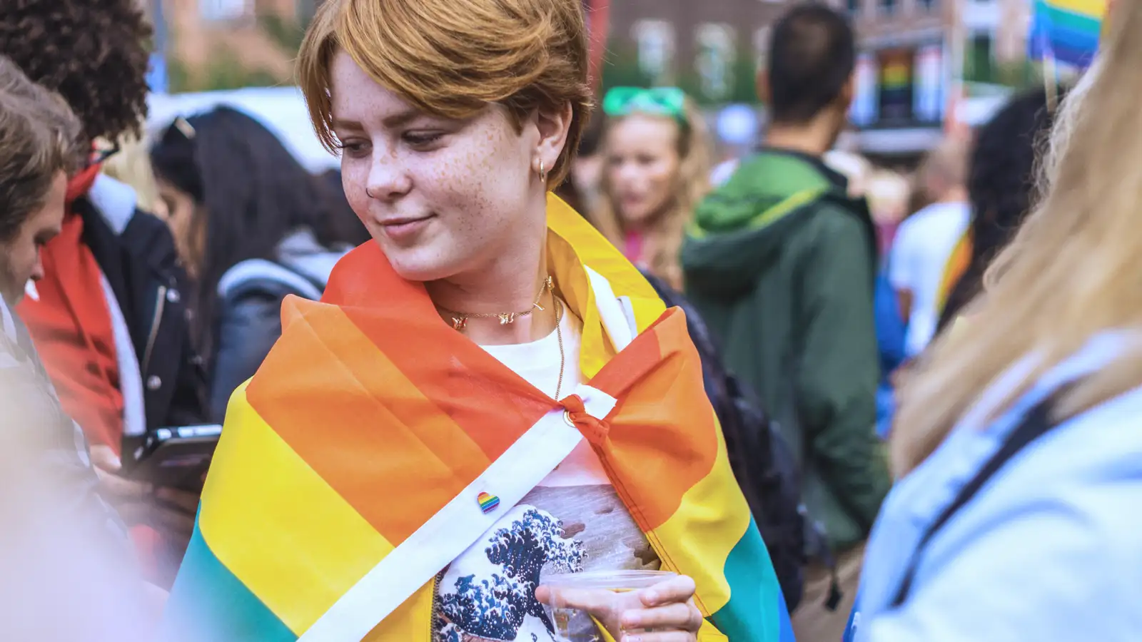 Ein junger Mensch mit einer umgehängten Regenbogenfahne.