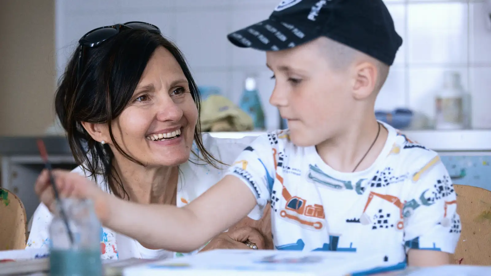 Ein Junge malt ein Bild und wird dabei von einer Frau begleitet.