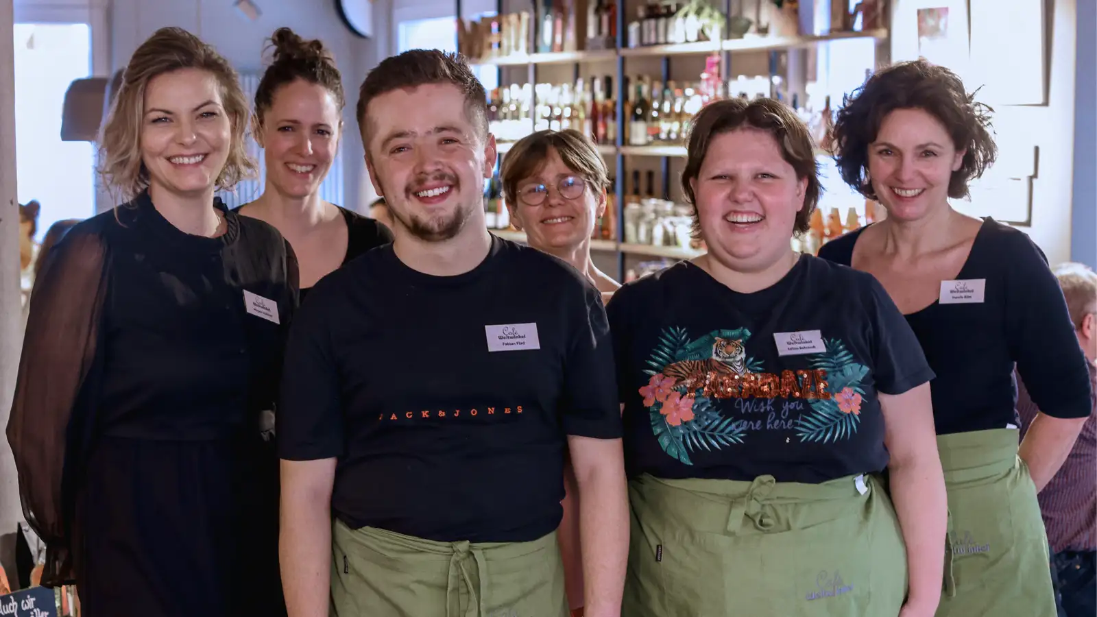 Eine Gruppe von Mitarbeiter*innen mit Schürzen in einem Café