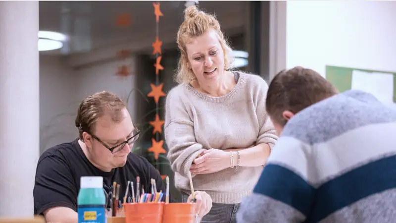 Drei erwachsene Personen beim Malen an einem Tisch