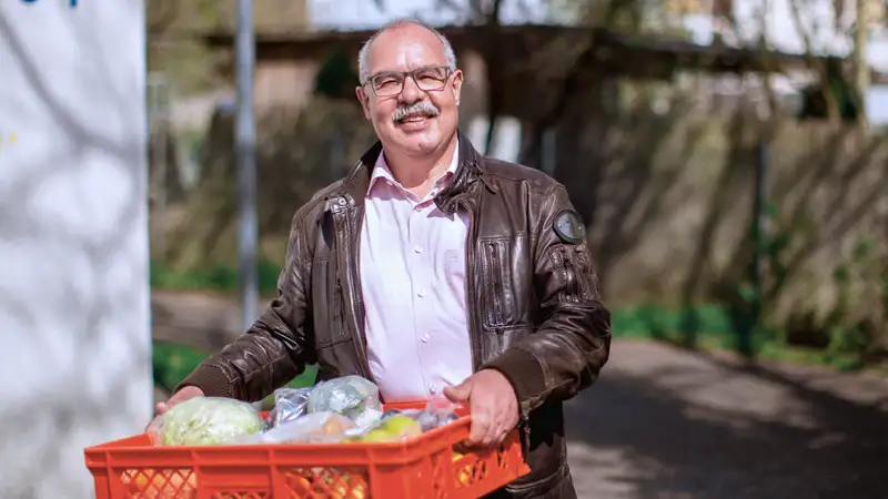Ein Mann trägt eine rote Kiste mit Obst und Gemüse.