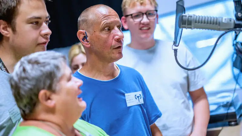 Vier Personen in einem Aufnahmestudio vor einem Mikrofon