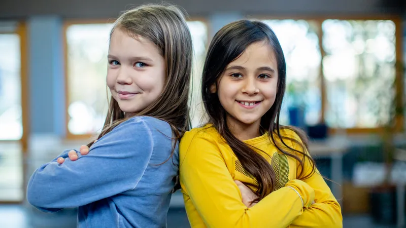 Zwei lächelnde Mädchen im Grundschulalter stehen Rücken and Rücken