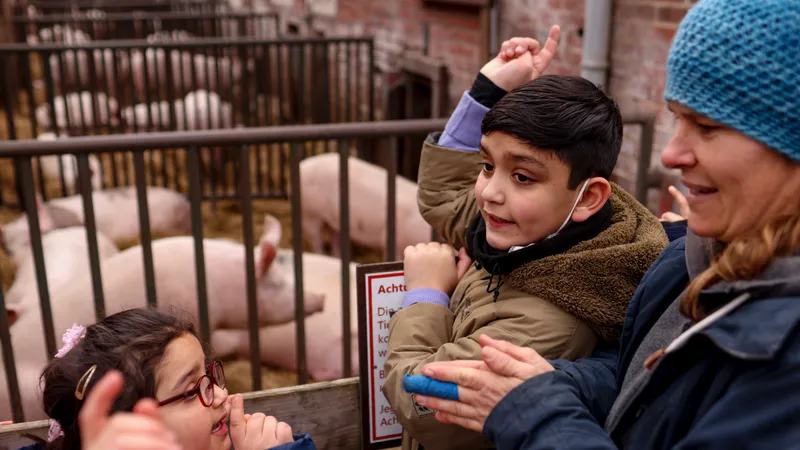 Zwei Kinder und eine Erwachsene in einem Schweinestall