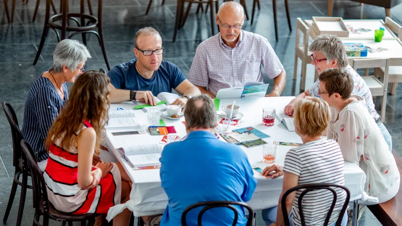 Eine Gruppe von acht Menschen sitzt an einem Tisch mit zahlreichen Prospekten und Unterlagen