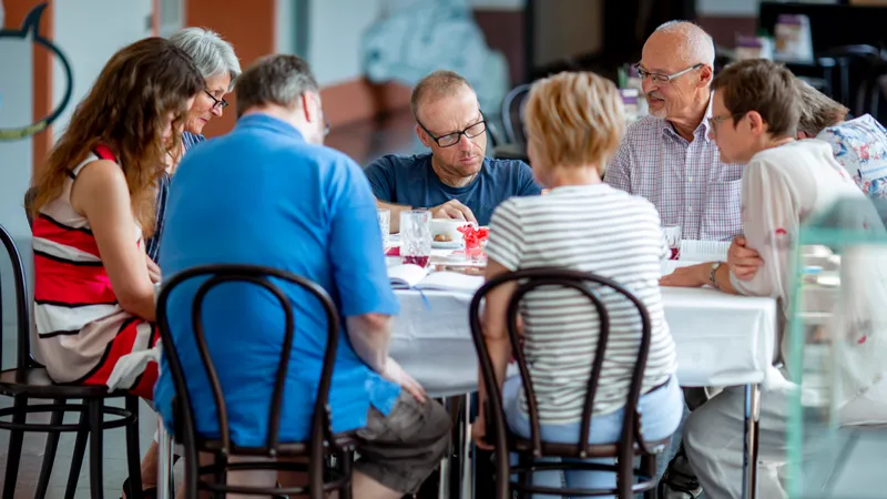 Eine Gruppe von acht Menschen sitzt an einem Tisch mit zahlreichen Prospekten und Unterlagen