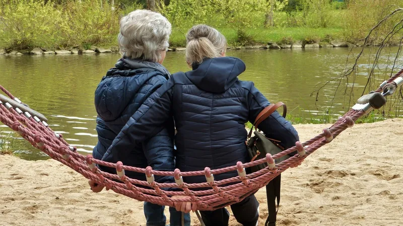 Zwei Frauen sitzen in einer Hängematte und blicken auf ein Gewässer.