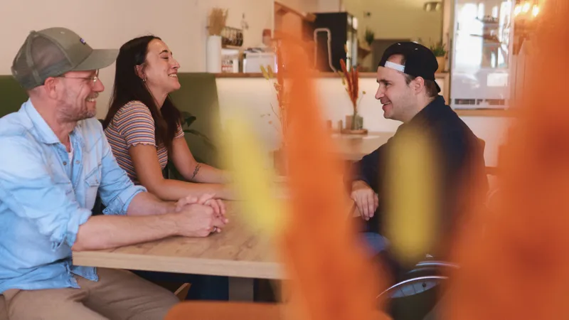 Eine Frau und zwei Männer unterhalten sich in einem Café