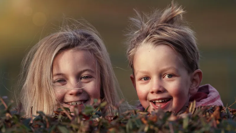 Zwei Kinder hinter einem Busch lachen in Richtung Kamera