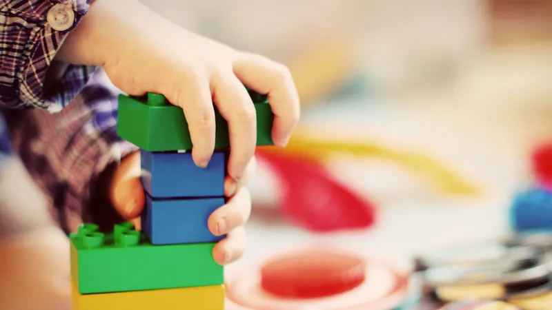 Eine Kinderhand beim Spielen mit bunten Klemmbausteinen