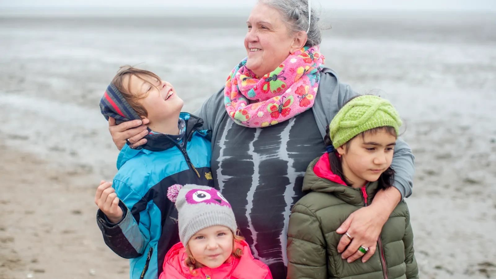 Eine ältere Frau mit derei Kindern an einem Strand
