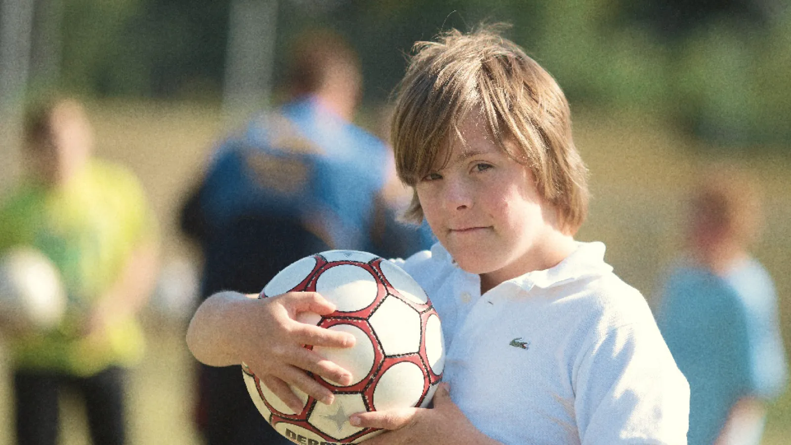 Ein Junge hält auf einem Sportplatz einen Fußball in den Armen