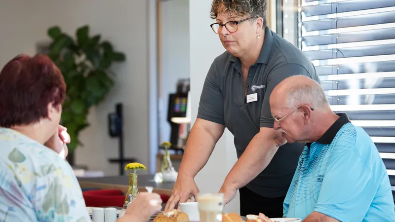 Eine Frau in einem Café serviert zwei Gästen ihr Frühstück