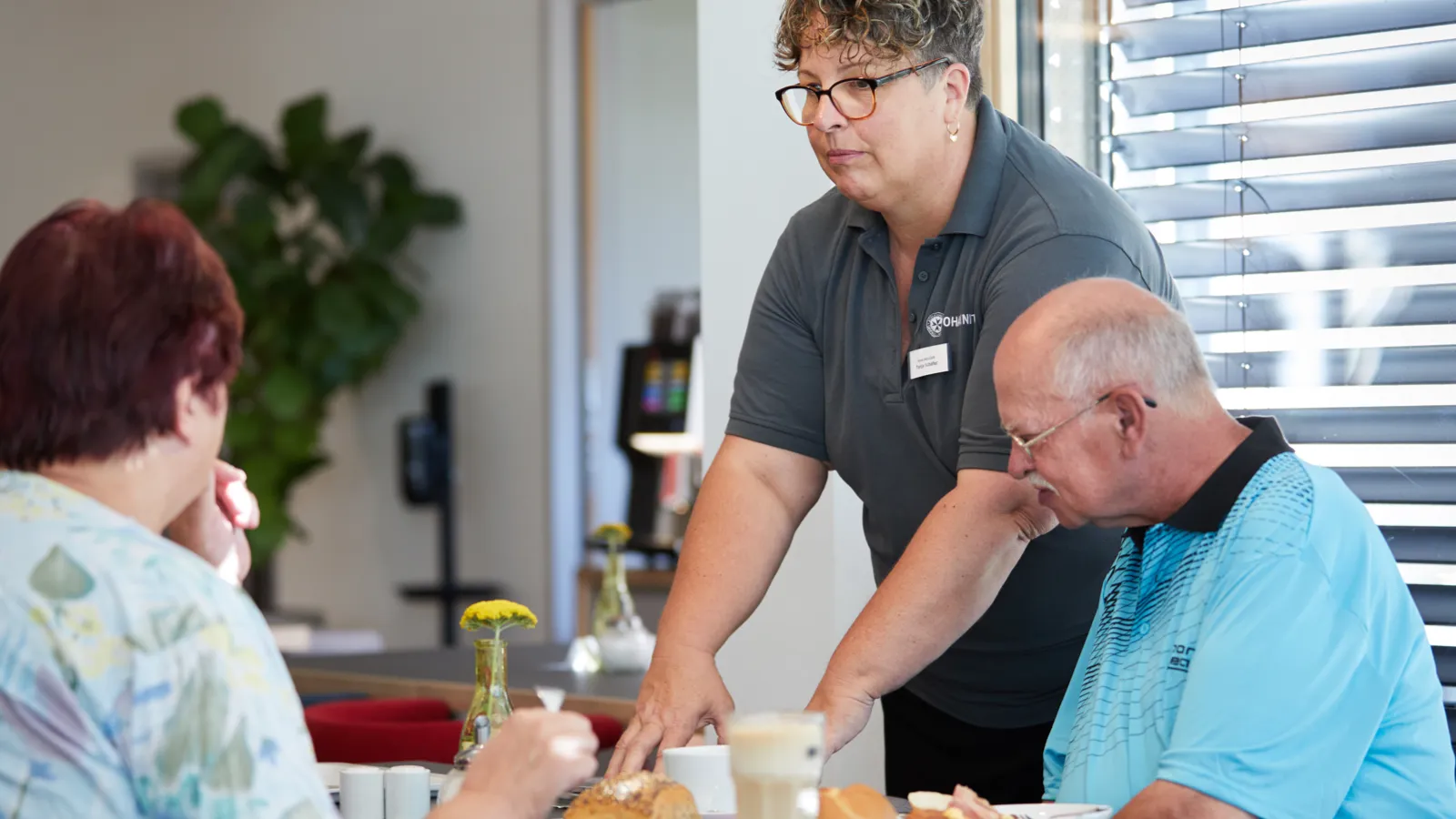 Eine Frau in einem Café serviert zwei Gästen ihr Frühstück