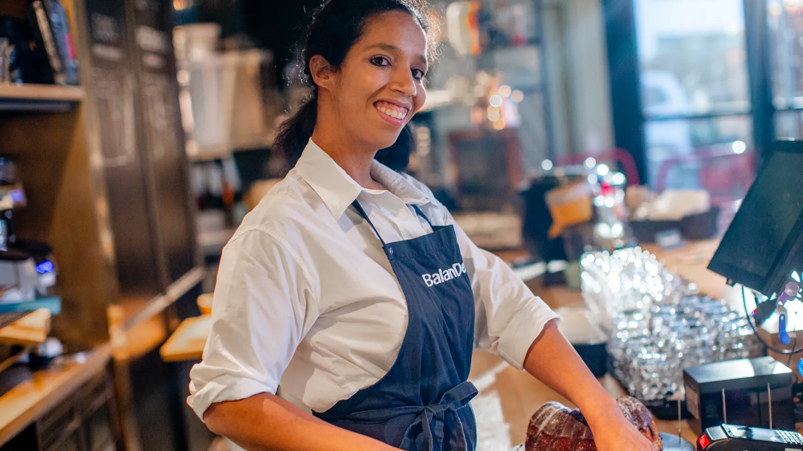 Eine junge Frau hinter dem Tresen eines Cafès schneidet einen Kuchen