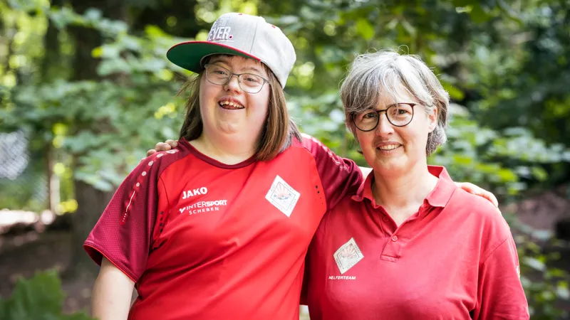 Eine Jugendliche mit Sporttrikot hält ihren Arm um eine Frau.